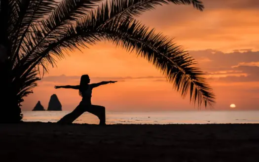 Una mujer practica yoga bajo las palmeras al atardecer
