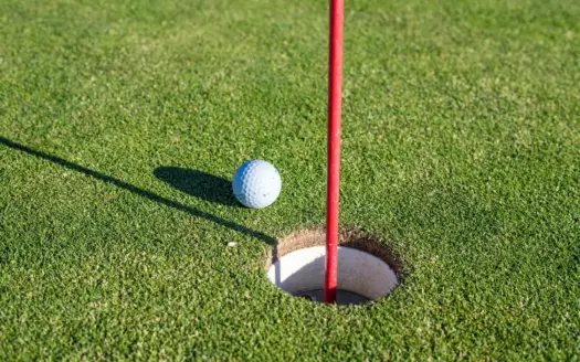 Bola de golf junto al hoyo en un green, con la bandera roja