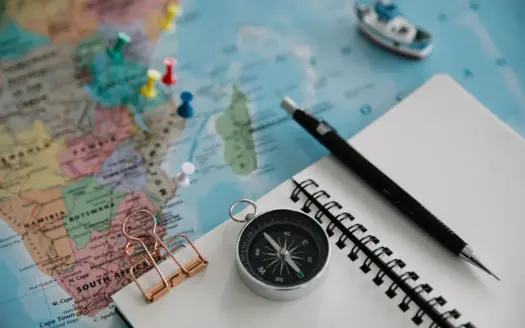 Mapa, brújula, cuaderno y bolígrafo sobre una mesa para planificar un viaje
