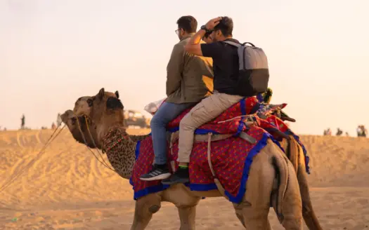Dos personas montan en camello por el desierto al atardecer