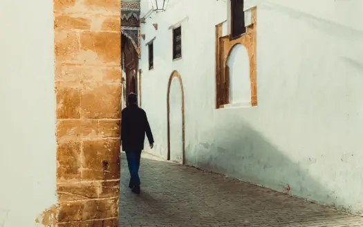 Una persona camina por un callejón soleado de arquitectura tradicional marroquí