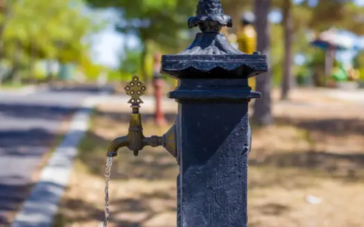 Grifo antiguo de agua en un día soleado, con un parque desenfocado al fondo