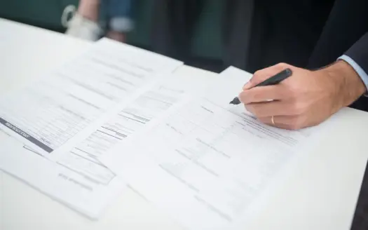 Una mano firma un documento de seguro sobre una mesa de oficina