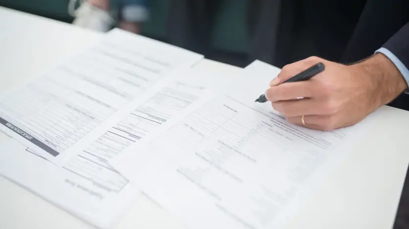 Una mano firma un documento de seguro sobre una mesa de oficina
