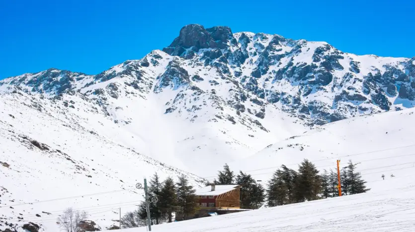 Laderas nevadas, un pilón de telesilla y chalés bajo un pico del Alto Atlas