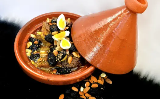 Tajine de cordero con ciruelas, almendras y huevo en un plato de barro